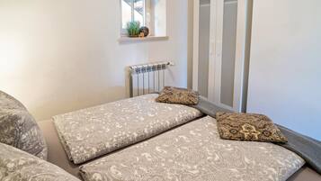 Un dormitorio con cama, almohadas, un radiador, una ventana y un armario.
