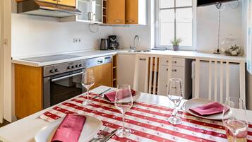 A modern kitchen with a stove, oven, and sink, a dining table set with a red and white tablecloth, and a window with a view.