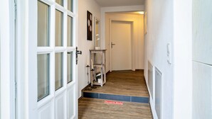 A hallway with white walls, wooden flooring, a door at the end, and a small shelf with a candle and a plant. - Holiday Apartment "2" with Mountain View, Shared Garden & Wi-Fi (Wallhausen)