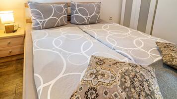 A neatly made bed with patterned bedding, a bedside table with a lamp, and a wooden floor.