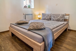 Un lit avec un cadre en bois, une couverture grise et des coussins à motifs.