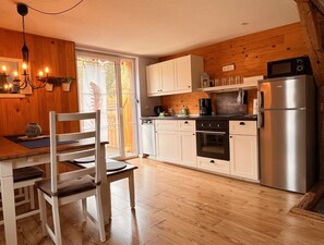 A kitchen with wooden cabinets, a stainless steel refrigerator, and a dining area with a table and chairs.