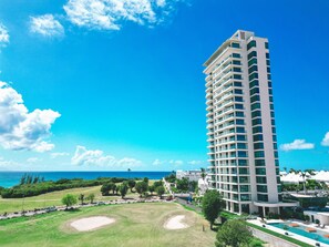 A tall hotel with a pool, surrounded by greenery and a clear blue sky. - B-505 (Cupecoy)