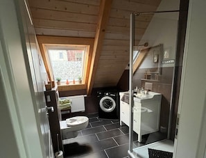 Ein kleines Badezimmer mit Waschmaschine, Toilette und Duschbereich.