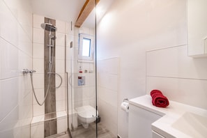 Et moderne badeværelse med et brusebadekabine i glas, toilet, håndvask og et vindue.