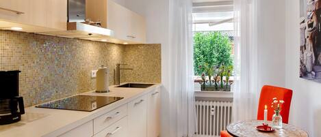 A modern kitchen with a tiled backsplash, a coffee machine, a sink, and a window with a view of greenery.