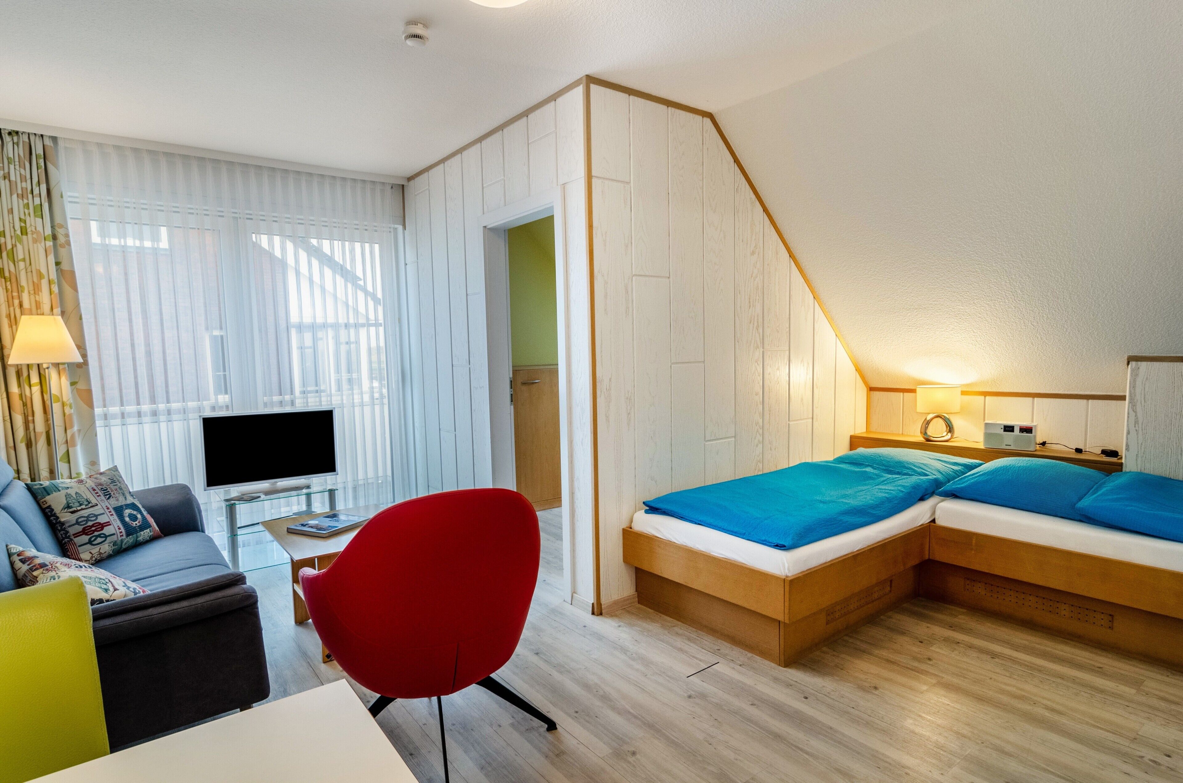 Une chambre d’hôtel moderne équipée d’un lit, d’une télévision, d’un bureau et d’un fauteuil rouge.