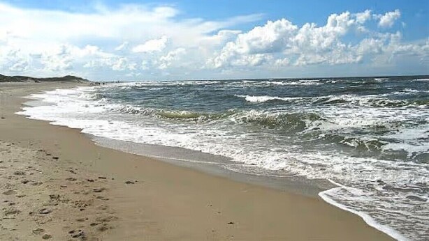 A beach with waves, a clear sky, and a distant shoreline. - Apartment 'Seestern - Wohnung 3' with Balcony and Wi-Fi (Norderney)