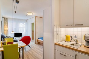 A compact hotel room with a kitchenette, a dining area with a table and chairs, a bed, and a TV. - Apartment 'Seestern - Wohnung 3' with Balcony and Wi-Fi (Norderney)