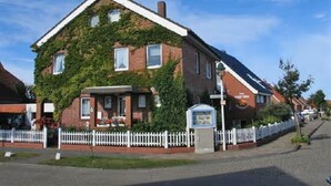 A two-story building with a sloped roof, a white picket fence, and a signboard. - Apartment 'Seestern - Wohnung 3' with Balcony and Wi-Fi (Norderney)