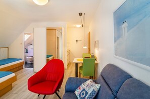 A compact room with a bed, a red chair, a blue sofa, a dining table, and a painting on the wall. - Apartment 'Seestern - Wohnung 3' with Balcony and Wi-Fi (Norderney)