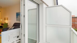 A room with a sliding glass door, a sofa with a cushion, a small table with a lamp, and a painting on the wall. - Apartment 'Seestern - Wohnung 3' with Balcony and Wi-Fi (Norderney)