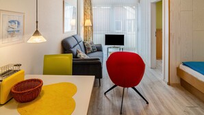 A modern living room with a sofa, a red chair, a television, and a dining area with a table and chairs. - Apartment 'Seestern - Wohnung 3' with Balcony and Wi-Fi (Norderney)