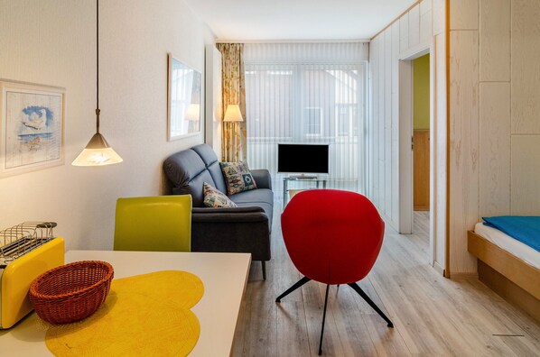 A modern living room with a sofa, a red chair, a television, and a dining area with a table and chairs. - Apartment 'Seestern - Wohnung 3' with Balcony and Wi-Fi (Norderney)