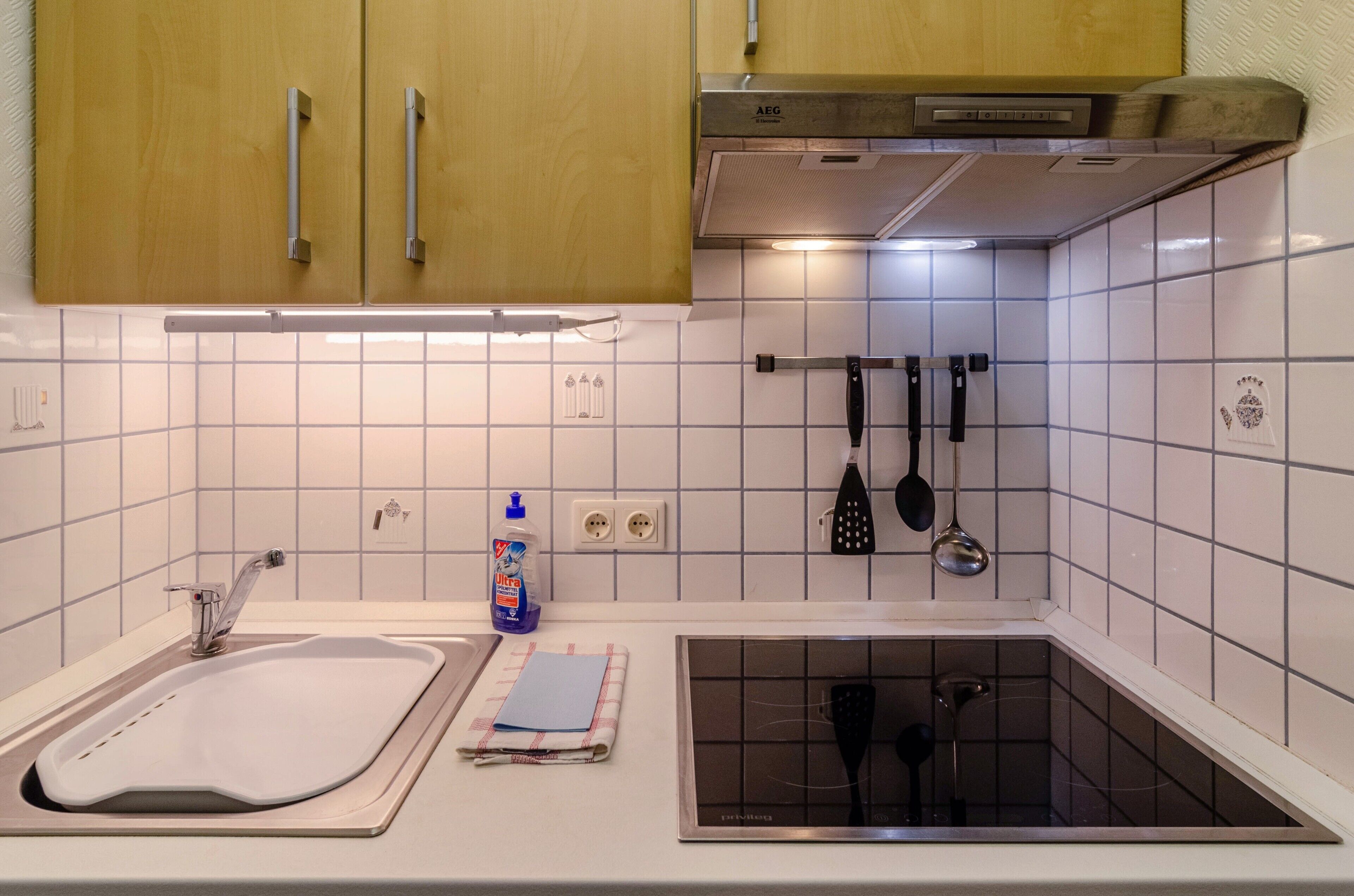 A kitchen with a double sink, wooden cabinets, a stainless steel range hood, and a tiled backsplash.