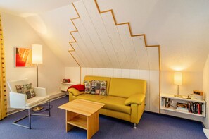 A room with a sofa, a chair, a small table, a bookshelf, and a unique zigzag ceiling design.