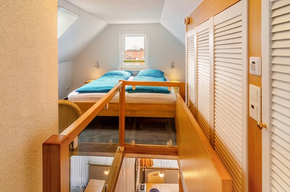 A dormitory-style room with a bunk bed, a window with blinds, a wooden door, and a staircase.