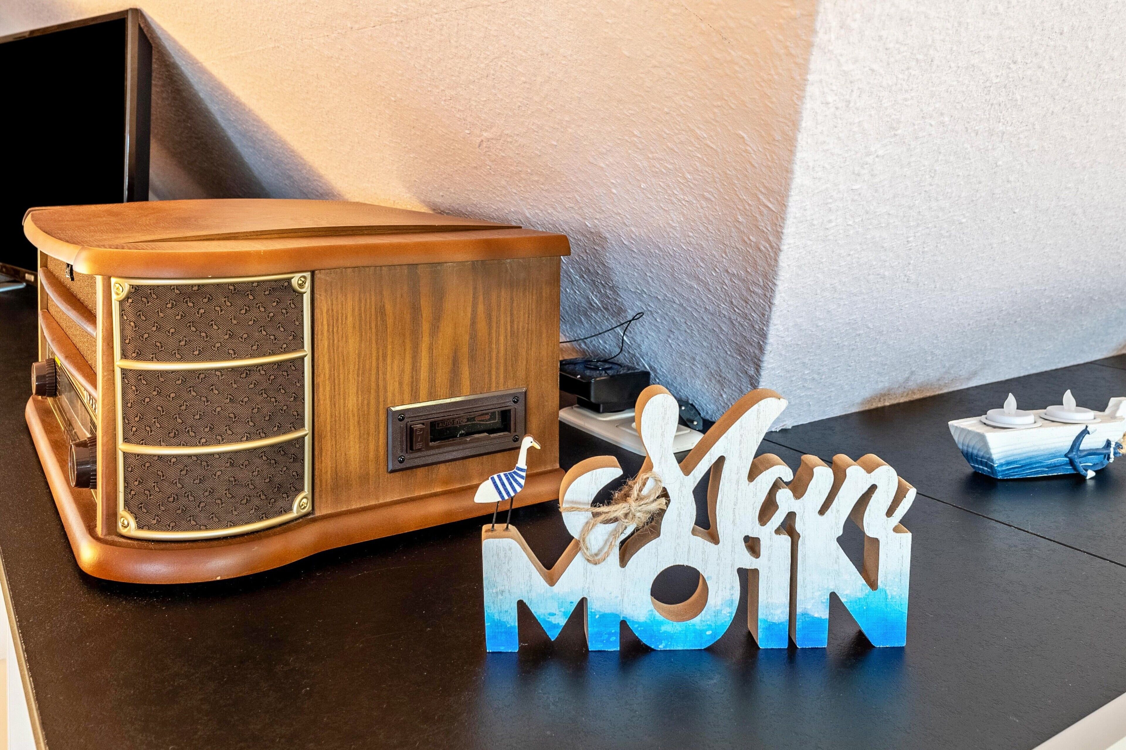 En gammal radio, en dekorativ skylt med texten ”MAMMA” och en liten fågelprydnad på ett bord.