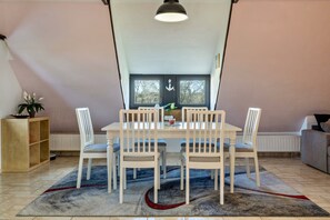 A dining area with a table, chairs, a rug, and a window with an anchor decoration.
