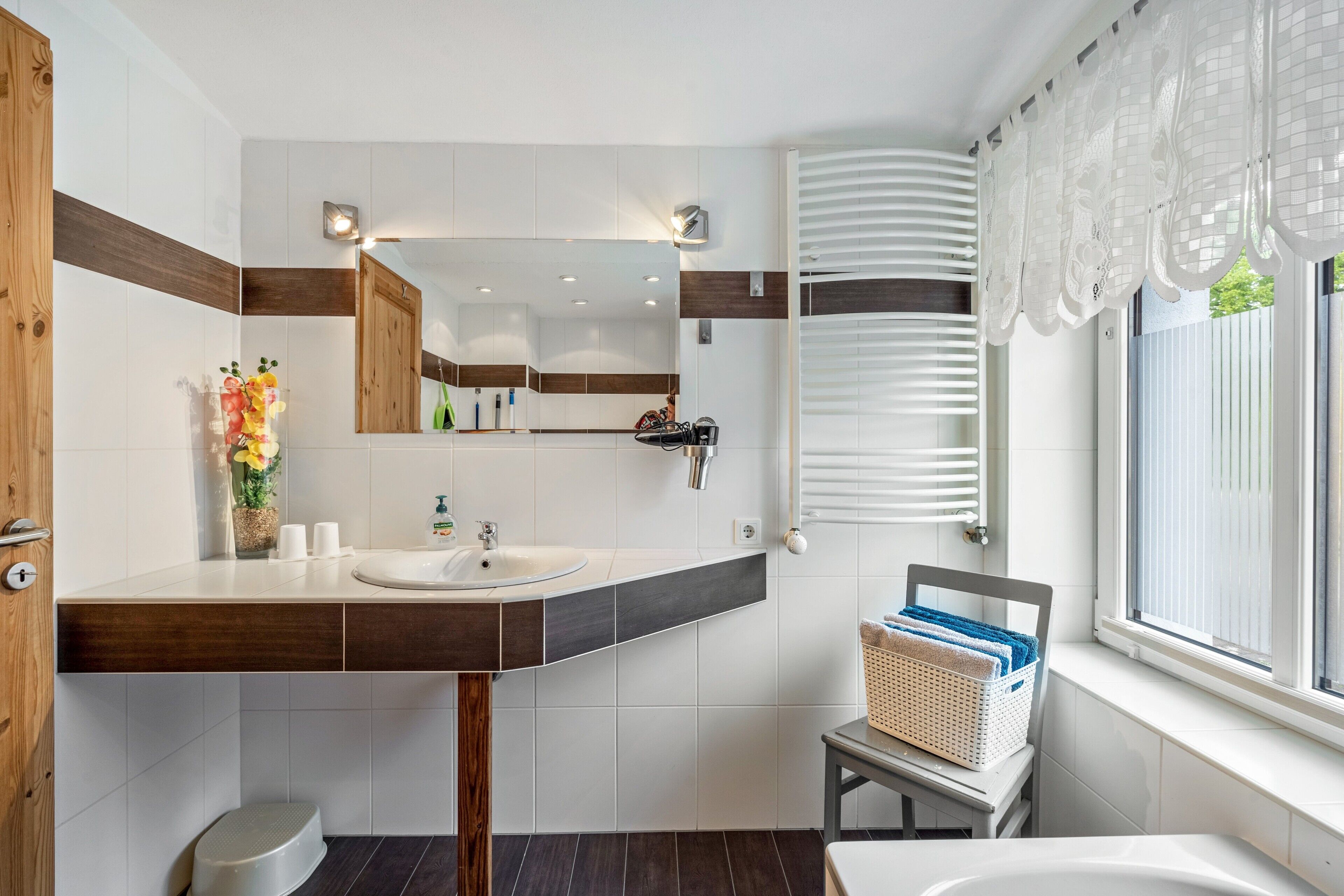 Un baño moderno con tocador de madera, un espejo grande, un lavamanos y una ventana con persianas.