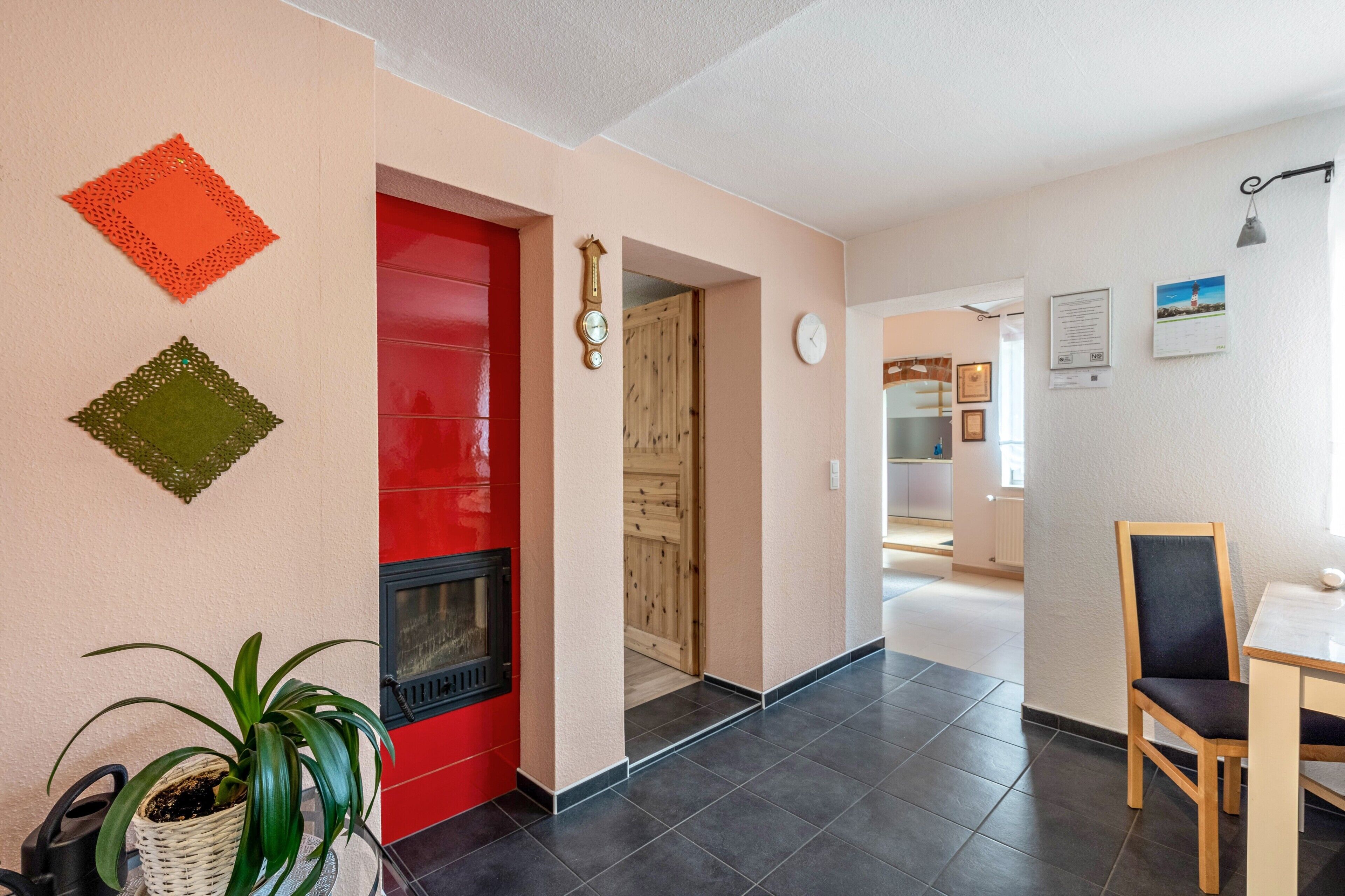 Un interior moderno con una puerta roja, una chimenea, una zona de comedor con una silla y un pasillo que conduce a otra habitación.