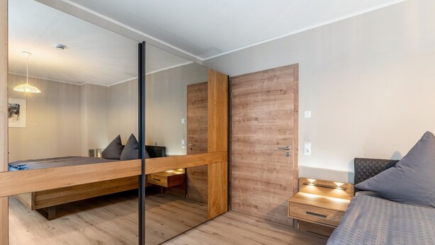 A modern bedroom with a wooden bed, a large mirror, and a wooden wardrobe. - Holiday Apartment 'Im Rosengarten 2' with Mountain View, Private Terrace and Wi-Fi (Zell am Harmersbach)