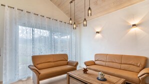 Una sala de estar con dos sofás de cuero marrón, una mesa de centro de madera, cortinas ligeras y lámparas colgantes.