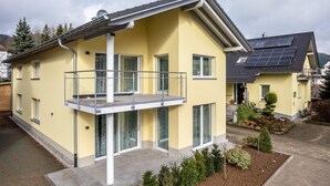 Una casa de dos pisos con balcón, paneles solares y jardín.
