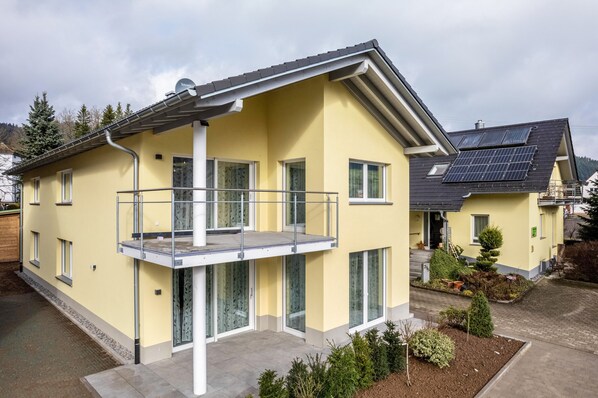Une maison à deux étages dotée d’un balcon, de panneaux solaires et d’un jardin.