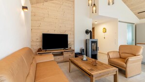 Una sala moderna con techo de madera, televisor de pantalla plana, sofás de cuero, una mesa de centro de madera e iluminación colgante.
