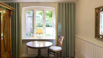 Een kamer met een ronde tafel, een stoel, een raam met gordijnen, een lamp en een spiegel aan de muur.