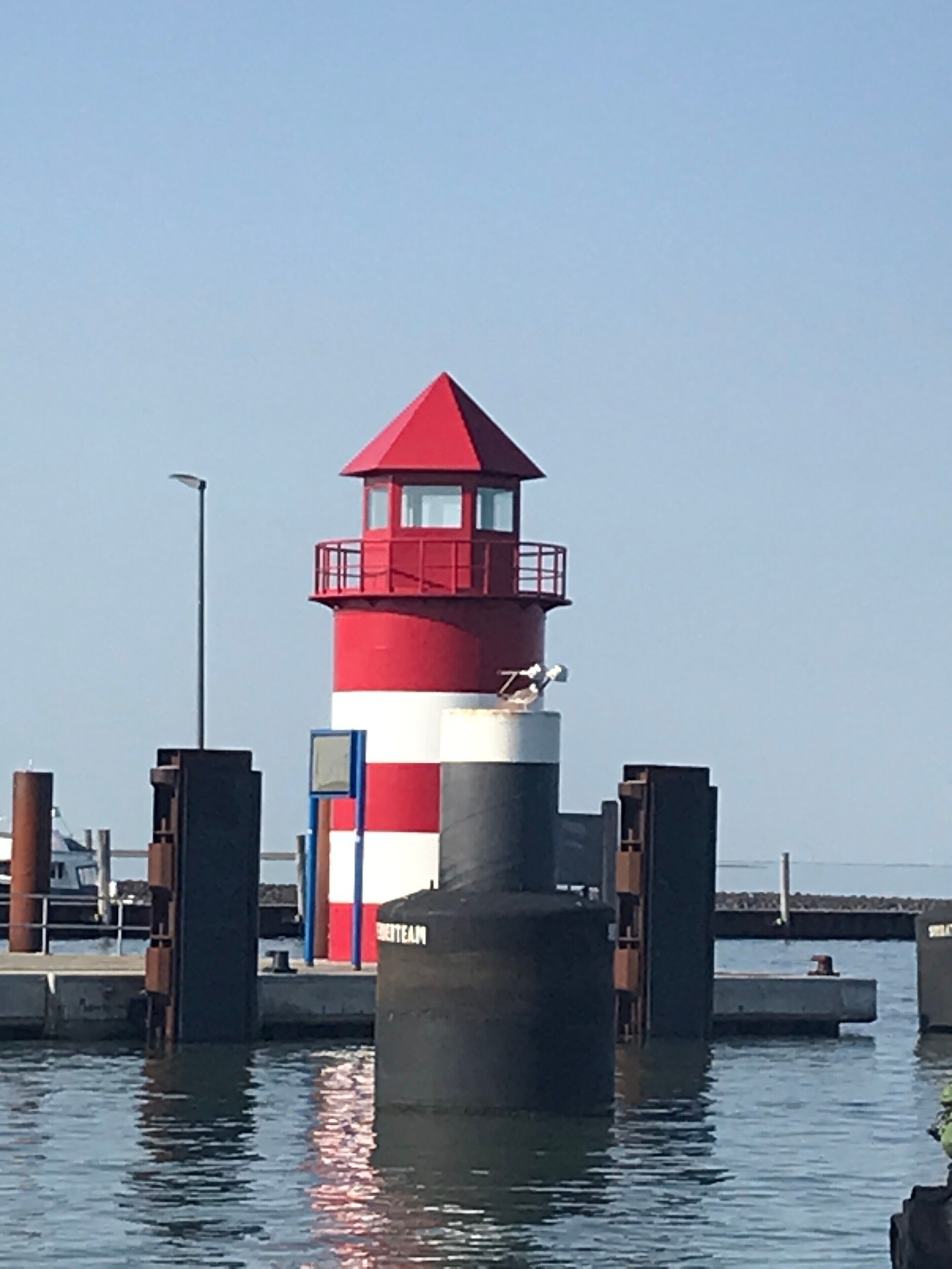 A lighthouse with a red and white striped tower, a small balcony, and a name plaque on the base.