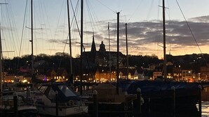 Een jachthaven met aangemeerde boten, kalm water dat de boten weerspiegelt, en een stad met gebouwen op de achtergrond.