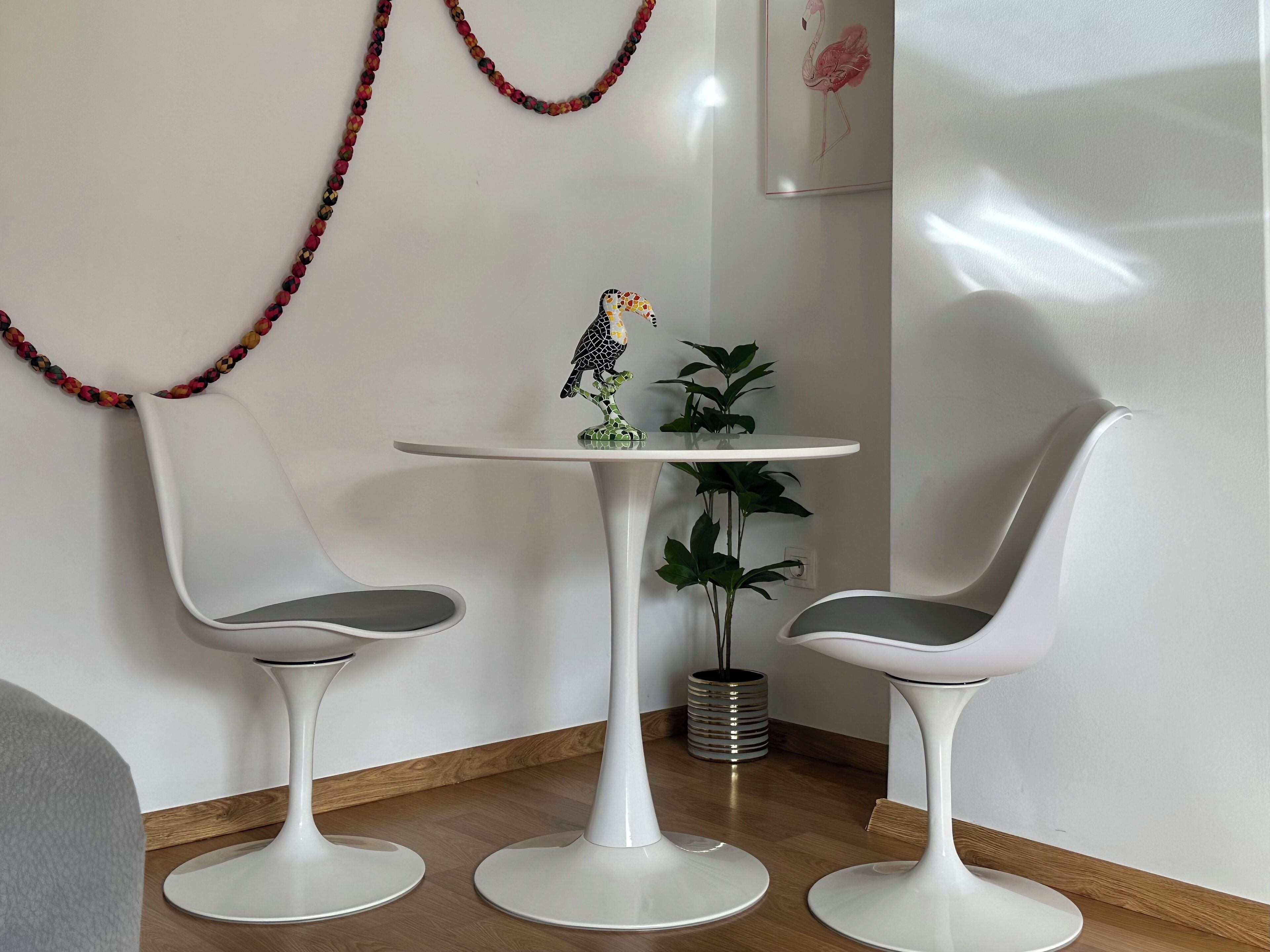 A modern room with two white chairs and a small round table, a decorative bird sculpture, and a framed artwork on the wall.