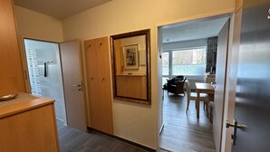 A hallway leading to a dining area with a table and chairs, a wooden door with a picture, and a window with a view of the outside.