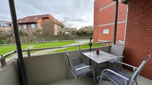 A balcony with a table and chairs, a brick wall, and a view of a grassy area with buildings in the background.