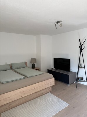A modern bedroom with a bed, TV, and a coat rack.