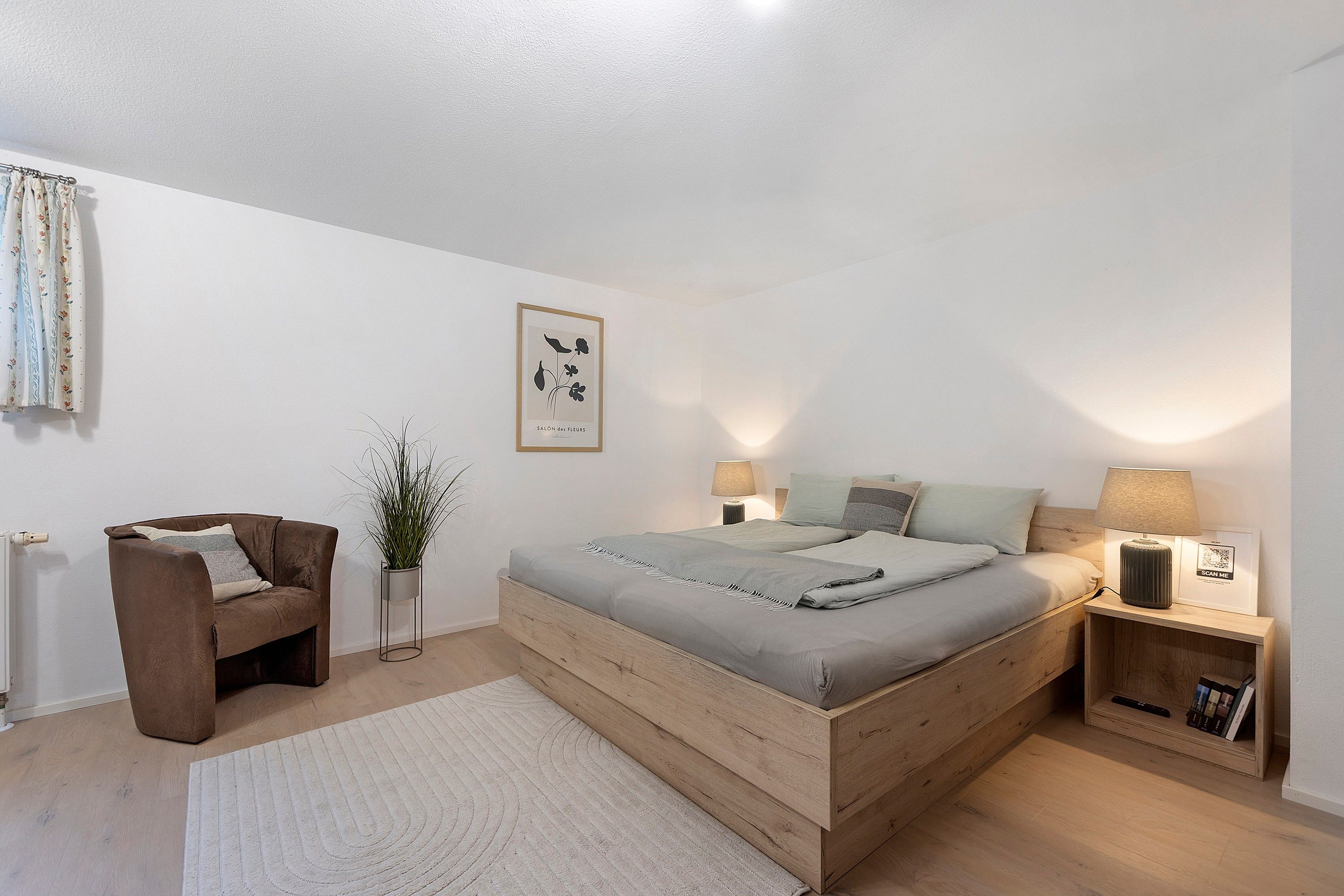 Une chambre à coucher avec un lit, des tables de chevet, une chaise, une plante et un tableau encadré au mur.