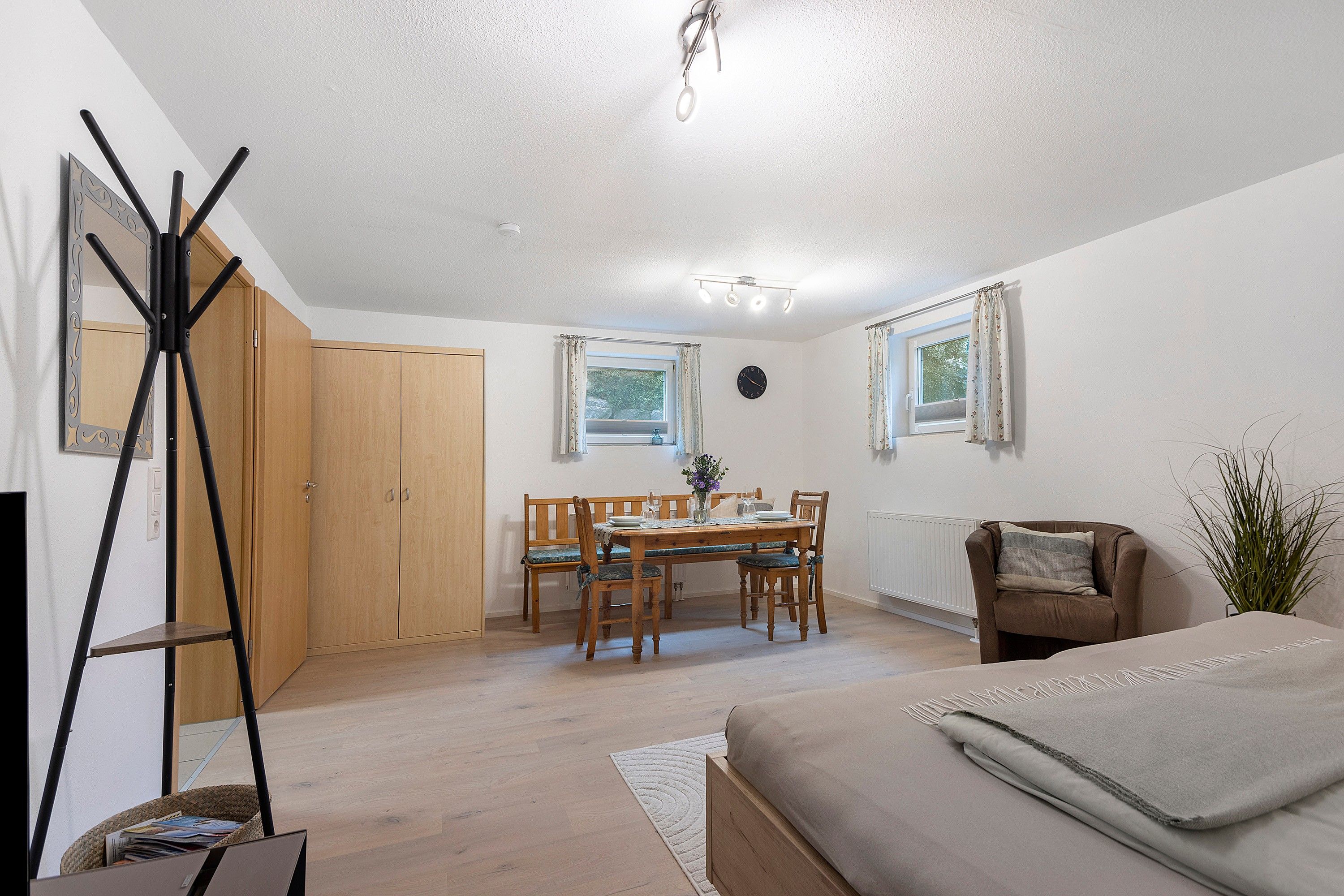 Une pièce comprenant un lit, une table à manger avec des chaises, un radiateur et une horloge au mur.
