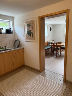 A kitchen with a microwave, sink, and a framed botanical illustration on the wall.