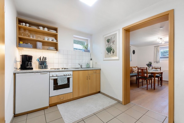 A compact kitchen with a Bosch dishwasher, a built-in oven, wooden cabinets, and a window above the sink.