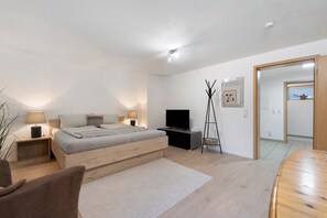 A modern bedroom with a bed, bedside tables, a TV, a mirror, and a wooden floor. - Holiday Apartment 'Locherer' with Wi-Fi (Wasserburg)