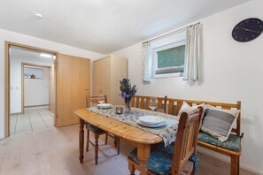 A dining area with a wooden table, chairs, a bench, a vase with flowers, a clock on the wall, and a window with curtains. - Holiday Apartment 'Locherer' with Wi-Fi (Wasserburg)