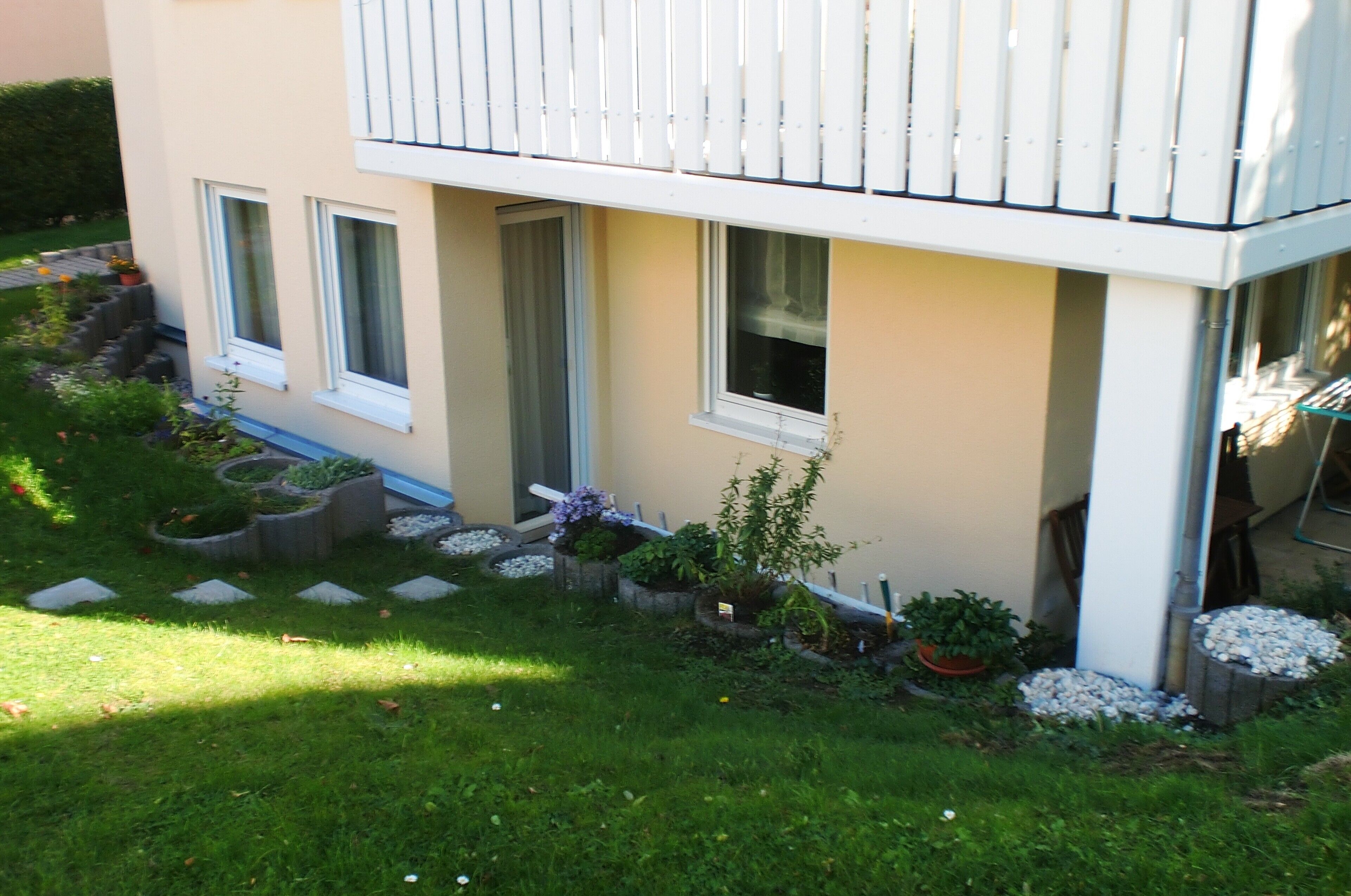 A building with a balcony, windows, and a garden with plants and stepping stones.