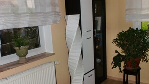 Et værelse med en radiator, et hvidt skab, en potteplante og et vindue med lette gardiner.