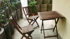 En lille terrasse med et træbord og to stole, omgivet af et lavt træhegn og krukker med planter.