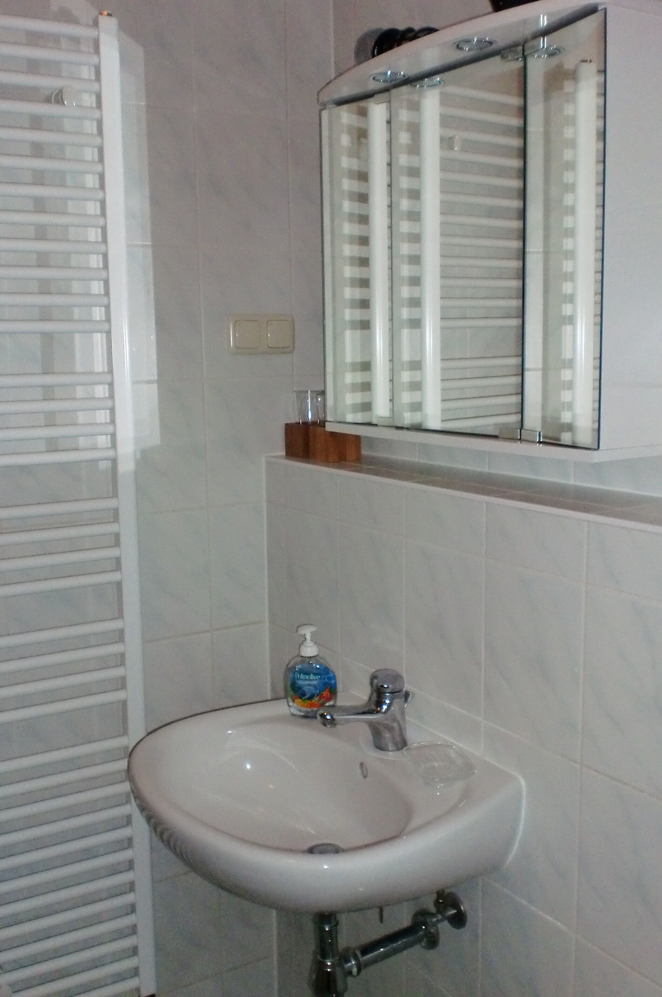 Un baño con un lavamanos blanco, un espejo y un perchero para toallas.