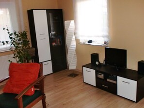 Une pièce comprenant une chaise en bois, un meuble noir et blanc, un téléviseur et une plante.