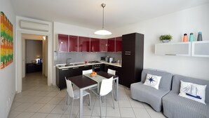 Une cuisine moderne avec des meubles de rangement rouges, un coin repas avec une table et des chaises, et un canapé gris agrémenté de coussins décoratifs.