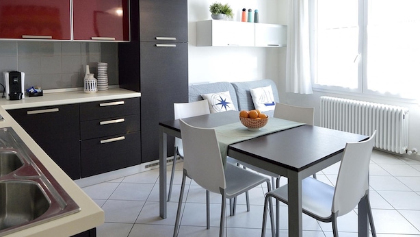 Une cuisine moderne avec des meubles de couleur sombre, un plan de travail blanc et un coin repas comprenant une table et des chaises.
